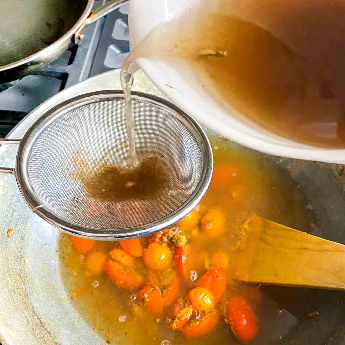 The tamarind water is being strained into the pot of rasam