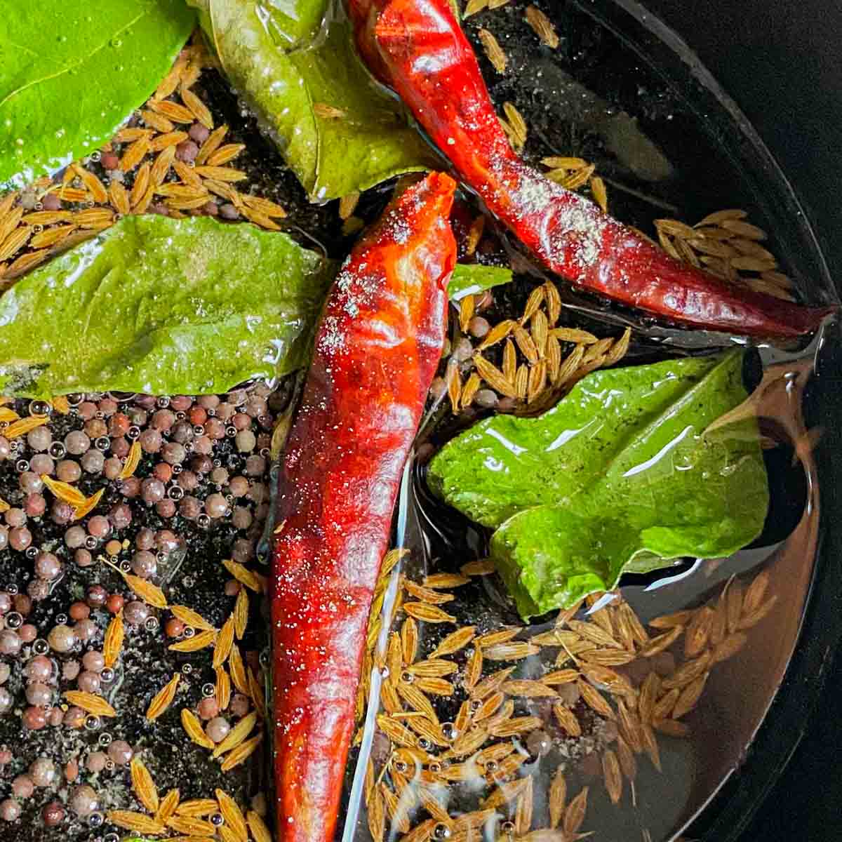 Curry leaves, cumin seeds, mustard seeds and chilis are being tempered in oil