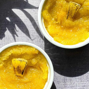 Pineapple kesari in white ramekins with charred pineapple slices and a shadow of pineapple