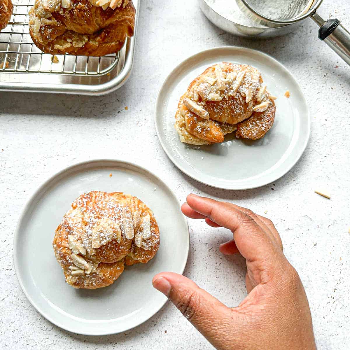 Badam halwa croissant on two plates. A hand reaching to grab a croissant.