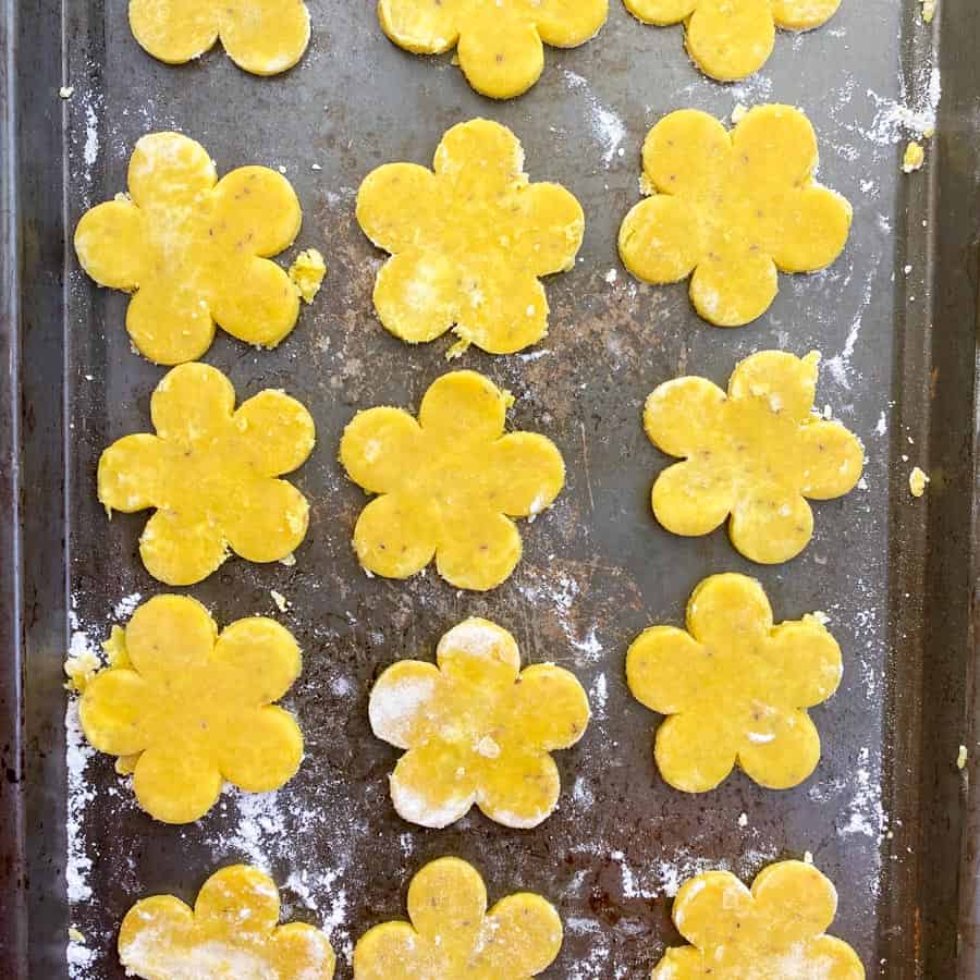 Yellow pie dough in the shape of sunflowers on the baking sheet dusted with flour