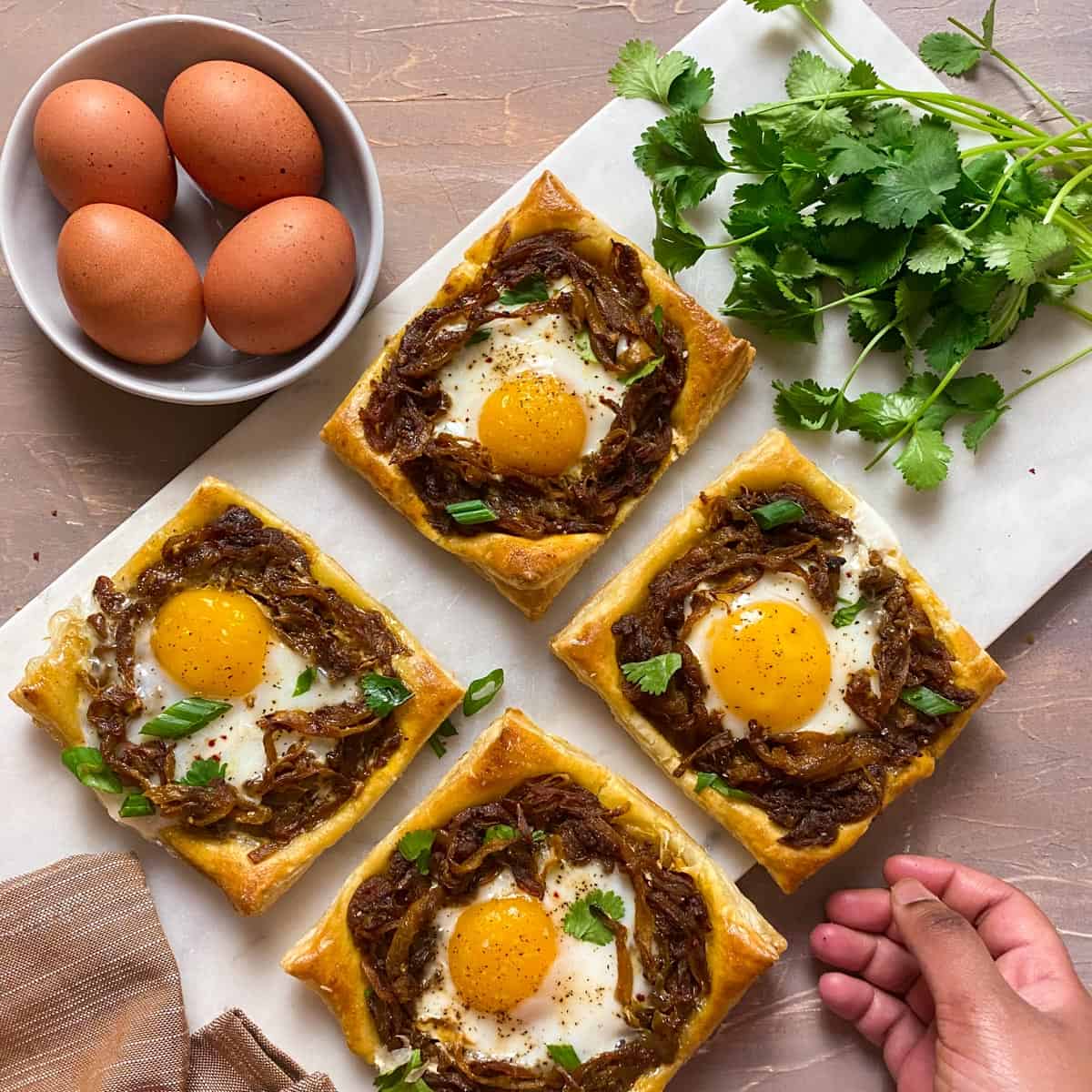 Caramelized onion masala tarts on a cutting board with a hand reaching for one
