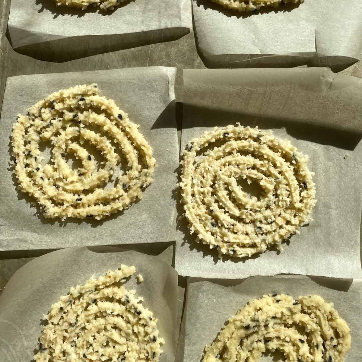 Raw murukkus on parchment paper for easy transfer