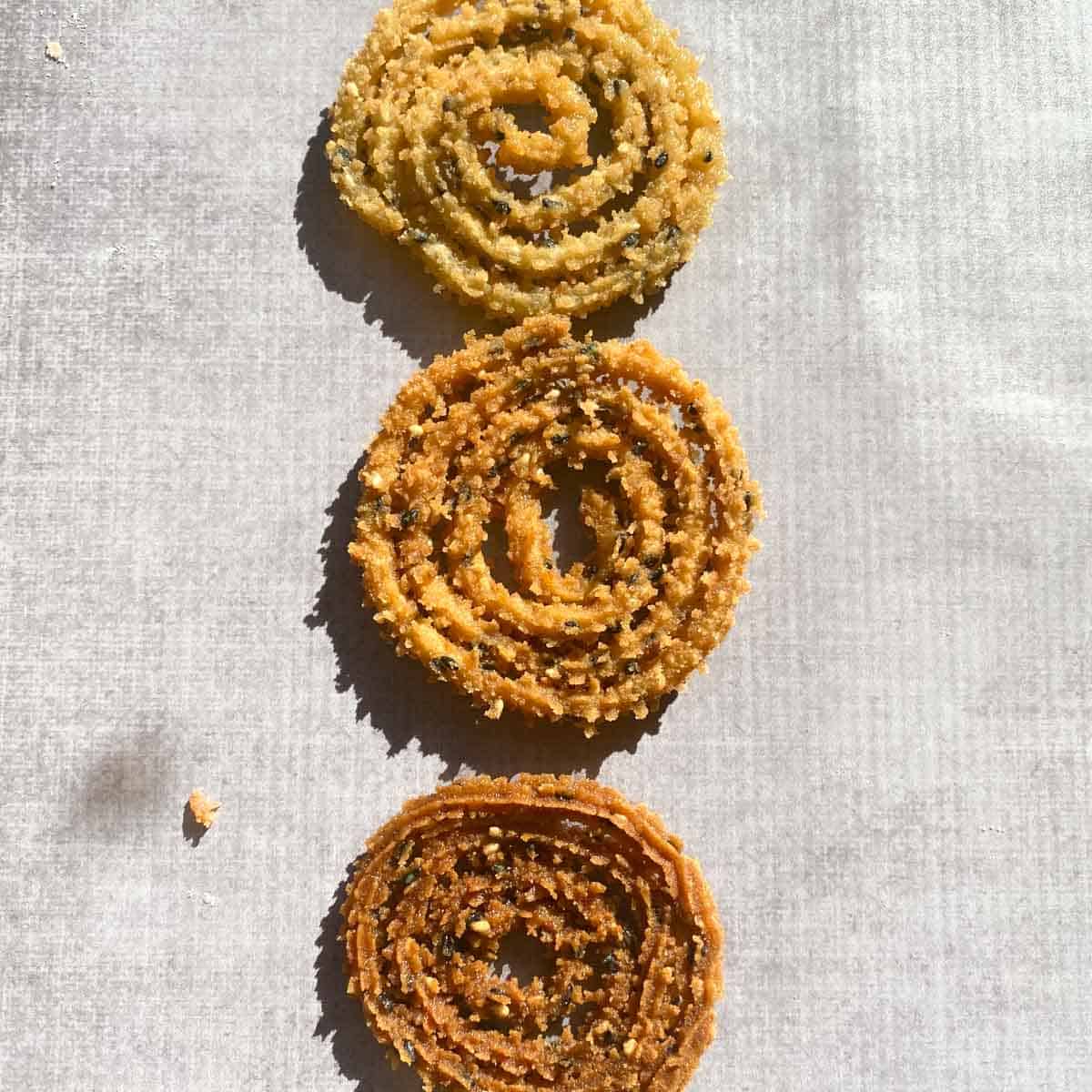 Picture of three murukkus of different shades. Top is undercooked, middle is properly cooked, and the bottom is overcooked