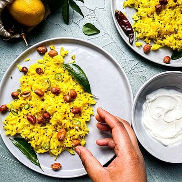 Lemon rice on plate with hand reaching to eat it. Yogurt on the side