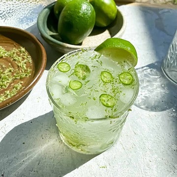 Nimbu pani cocktail with limes and lime zest in the background