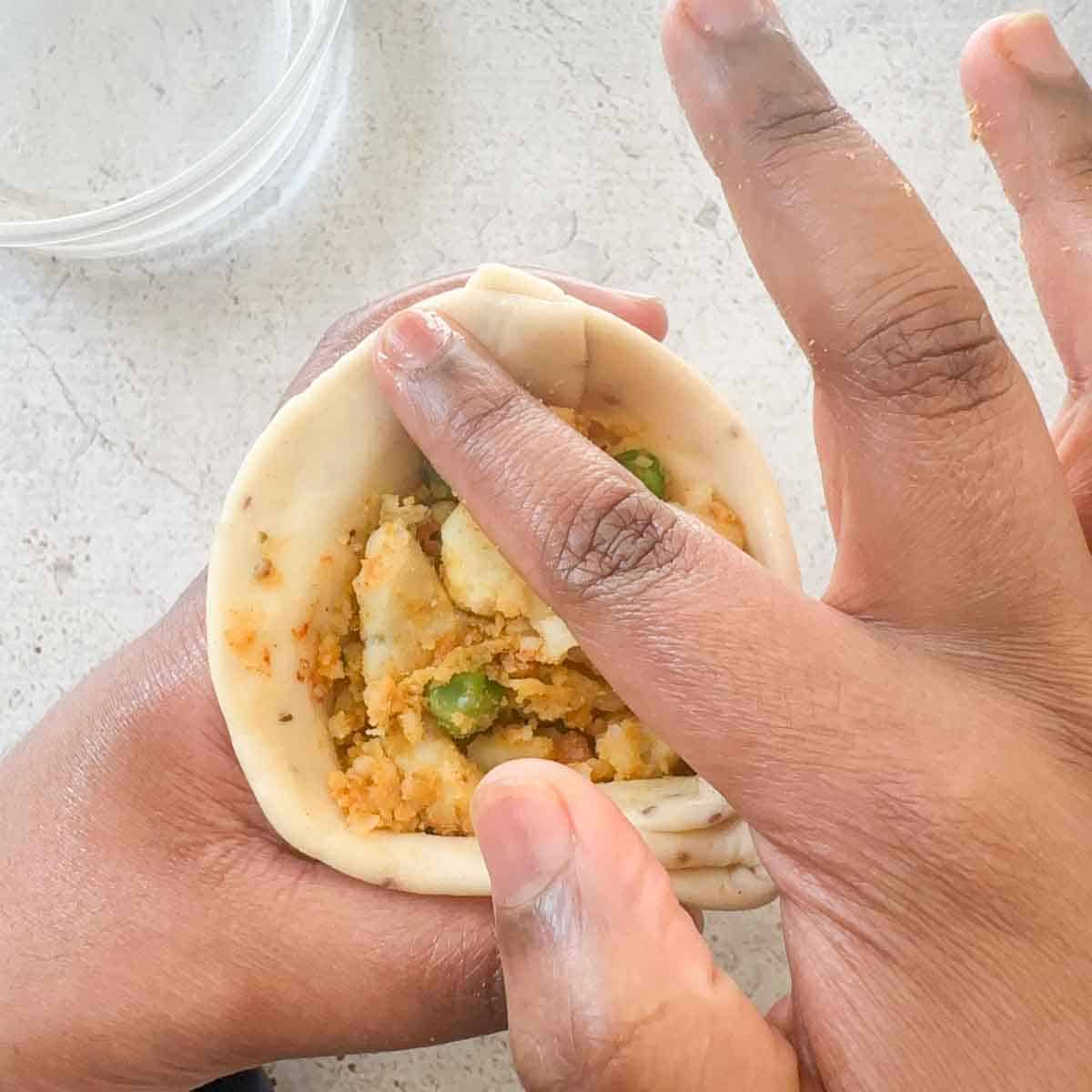 Water being used on the index finger to wet seams of samosa dough.