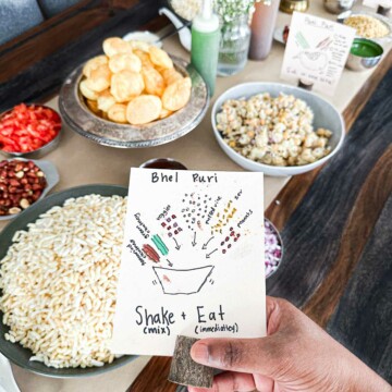 A close up of table decor for a chaat party. It includes a sign for how to make bhel puri as well as ingredients for chaat in the background.