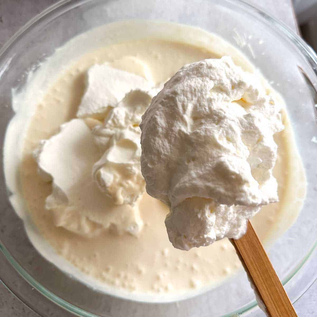 Whipped cream being folded into a bowl of condensed milk