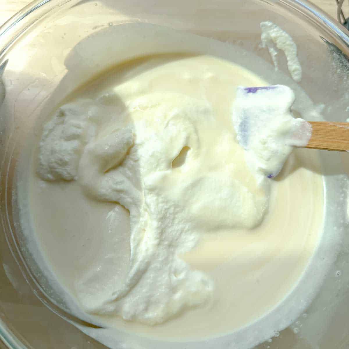 Folding in airy whipped cream into a thick condensed milk base