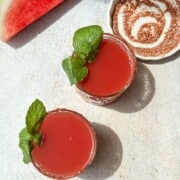 Two glasses of watermelon juice with chaat masala with a spiced rim and mint garnish.