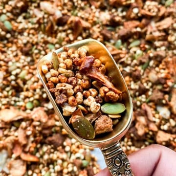 Chai spiced granola in a mini scoop. The granola has golden puffed millets pepitas, and toasted coconuts. The background has a sheet tray with granola.