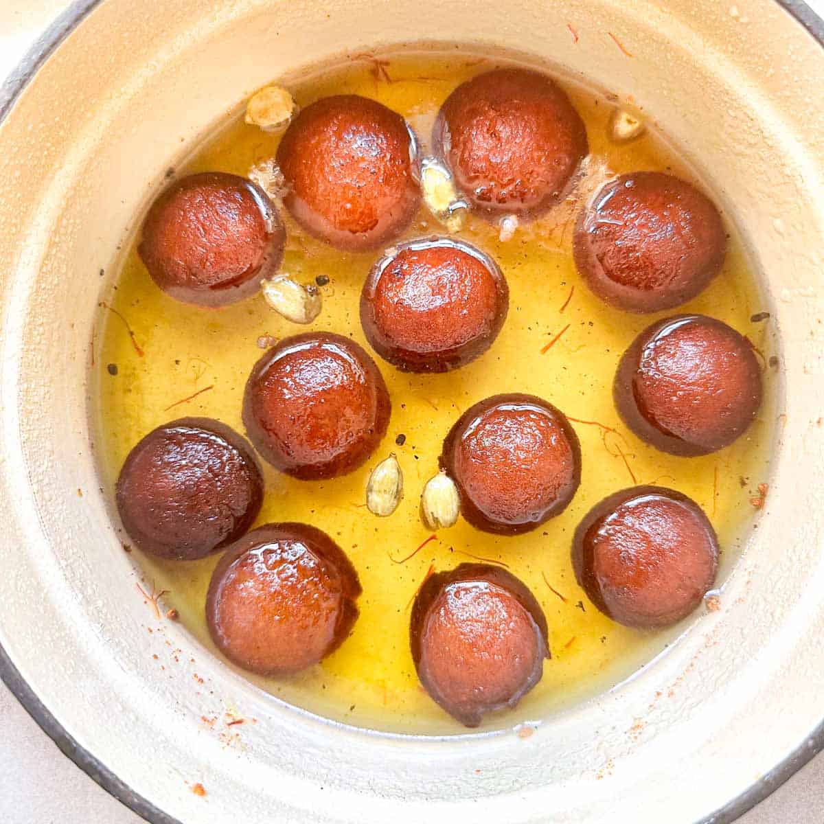 Gulab jamun balls made with milk powder in a deep bowl with cardamom saffron syrup.