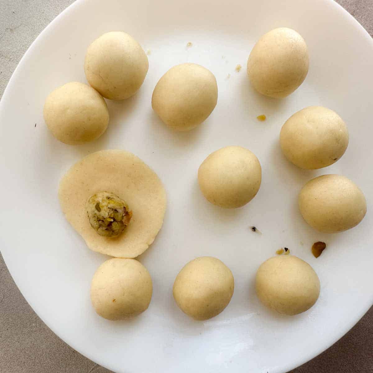 Plate of stuffed gulab jamun. One jamun is not yet formed and has the plain dough rolled into a disc and pistachios in the center.