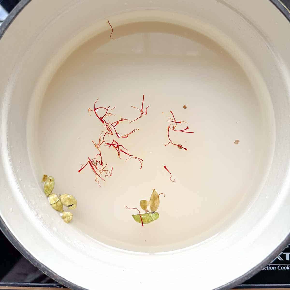 Pot with gulab jamun syrup ingredients like saffron, sugar, water, and cardamom