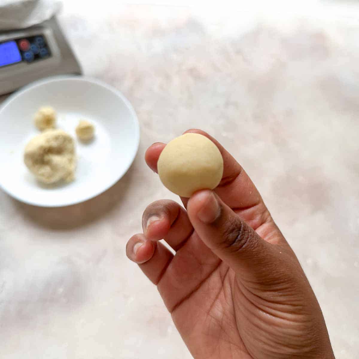 A hand holding a rolled gulab jamun dough