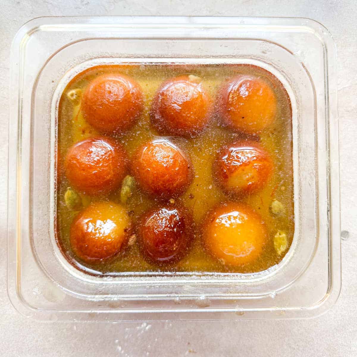 Gulab jamuns stored in a square and clear plastic container