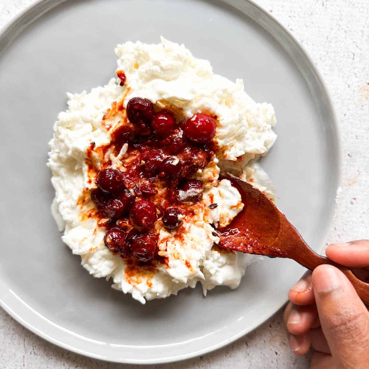 Yogurt rice with cranberry achar on top. A brown hand scooping some rice and achar.