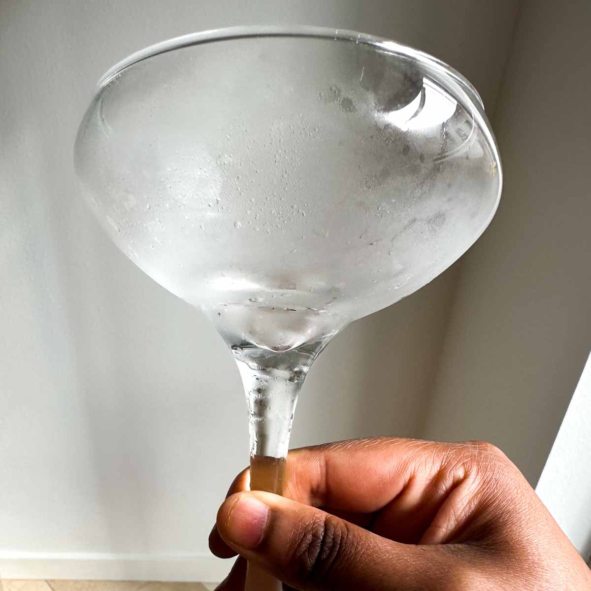 A brown hand holding a chilled coupe glass.