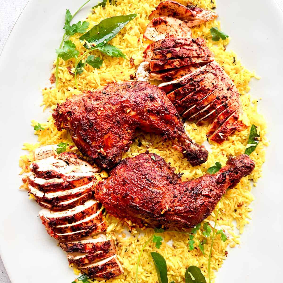 Whole tandoori chicken that is cut and served on a large platter on top of lemon rice.