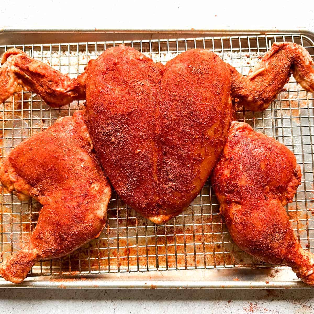 A spatchcocked tandoori chicken on a wire rack sheet tray with a dry rub.