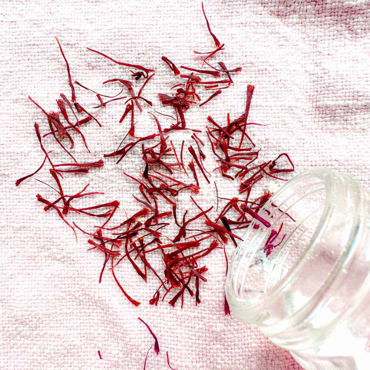 Saffron threads poured out from a glass bottle on a pink towel