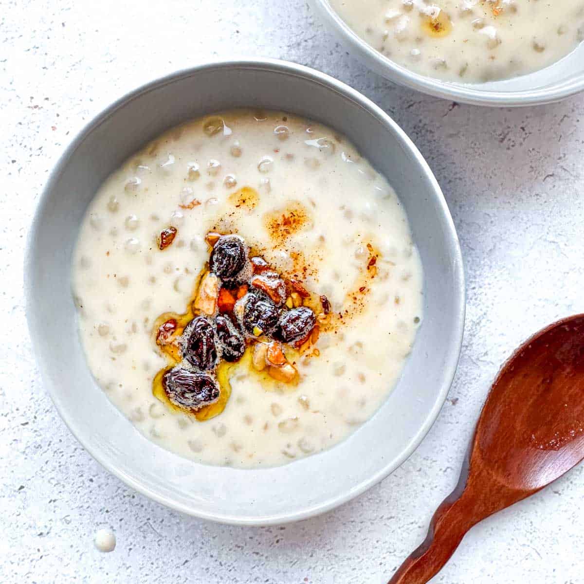 Two bowls with Indian tapioca pudding with a nut and raisin topping. A wooden spoon on the bottom right.