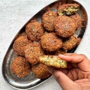 A hand holding a cut open masala vada. Other golden masala vadas resting on a sliver platter.