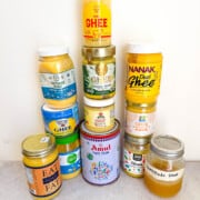 11 different ghee brand jars and 1 homemade ghee jar all lined up in a pyramid.