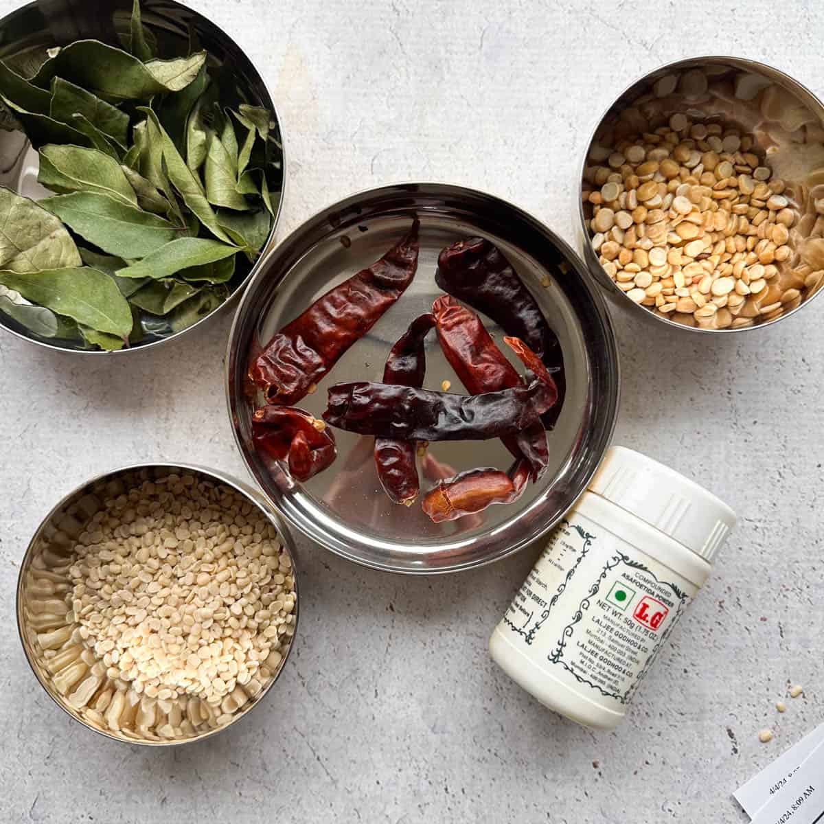 5 ingredients needed to make milagai podi or Indian gunpowder. Pictured are bowls of curry leaves, chana dal, split and hulled urad dal, dried red Indian chilis, and asafoetida.