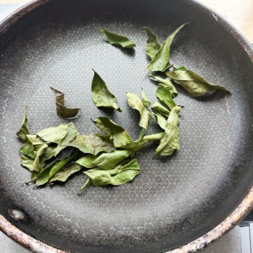 Curry leaves dry roasting on a skillet until dried out.
