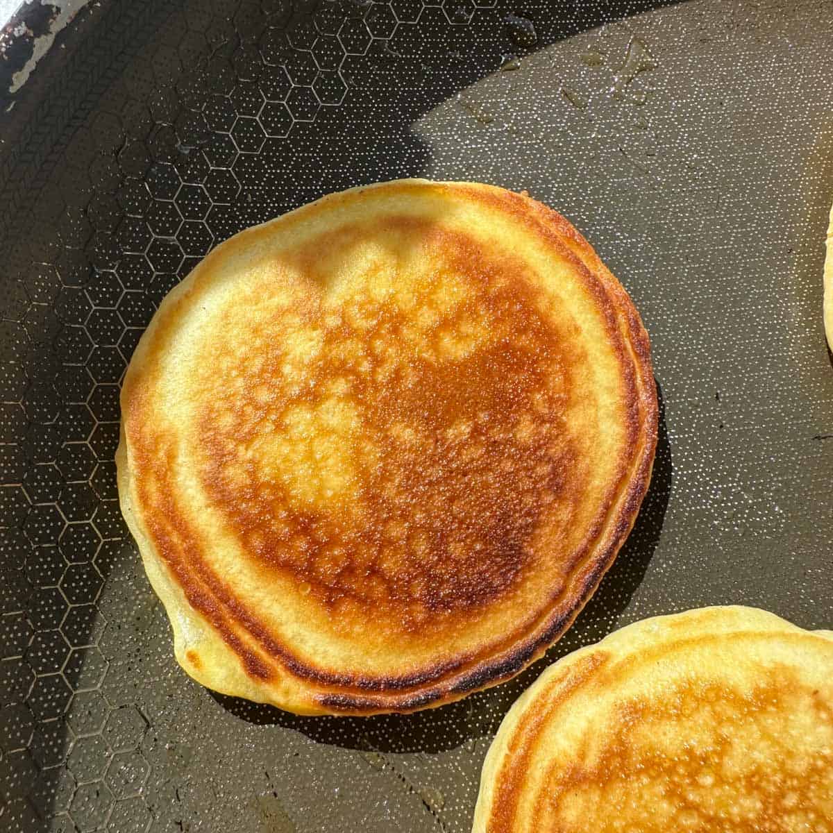 A golden pancake on a pan with other mini pancakes.