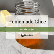 Ghee in a glass mason jar in the forefront. Stick of butter on a white board in the background.