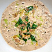 Black eyed peas curry with coconut milk in a large white bowl. The top of the curry has curry leaves, cumin seeds, and mustard seeds.