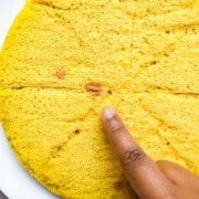 A finger pointing to red spots in the cooked dhokla. These spots indicate pockets of baking soda build up in the dhokla.