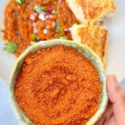 Pav bhaji masala or spice blend in a small bowl. A fully prepared dish of pav bhaji displayed in the background made with the spice blend.