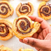 A hand holding a baked and crispy caramelized onion puff pastry pinwheel.