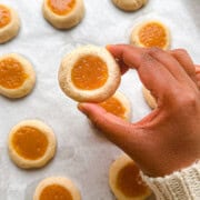 A hand holding baked cardamom thumbprint cookies filled with a mango curd.
