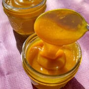 Mango curd in two glass jars with a spoon scooping up the thick mango curd.