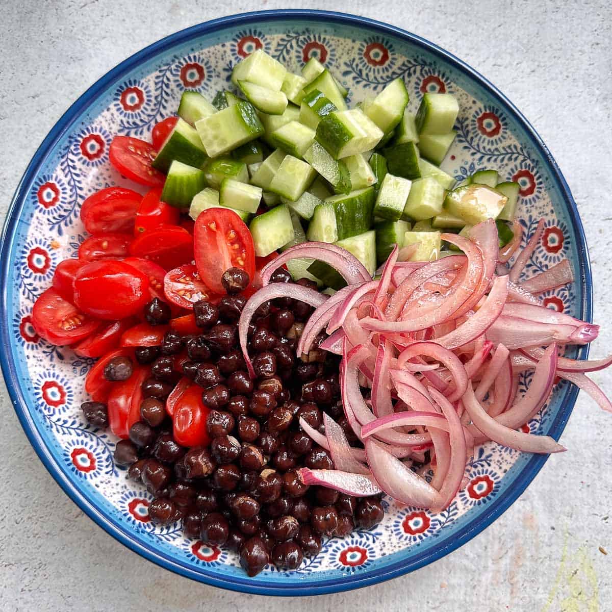 A bowl with black chickpeas, sliced cherry tomatoes, cucumbers, and pickled onions.