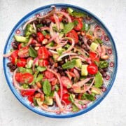 A bowl filled with a kala chana or chickpea salad. The salad has black chickpeas, pickled onions, cucumbers, tomatoes, mint, cilantro, and toasted peanuts.