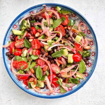 A bowl filled with a kala chana or chickpea salad. The salad has black chickpeas, pickled onions, cucumbers, tomatoes, mint, cilantro, and toasted peanuts.