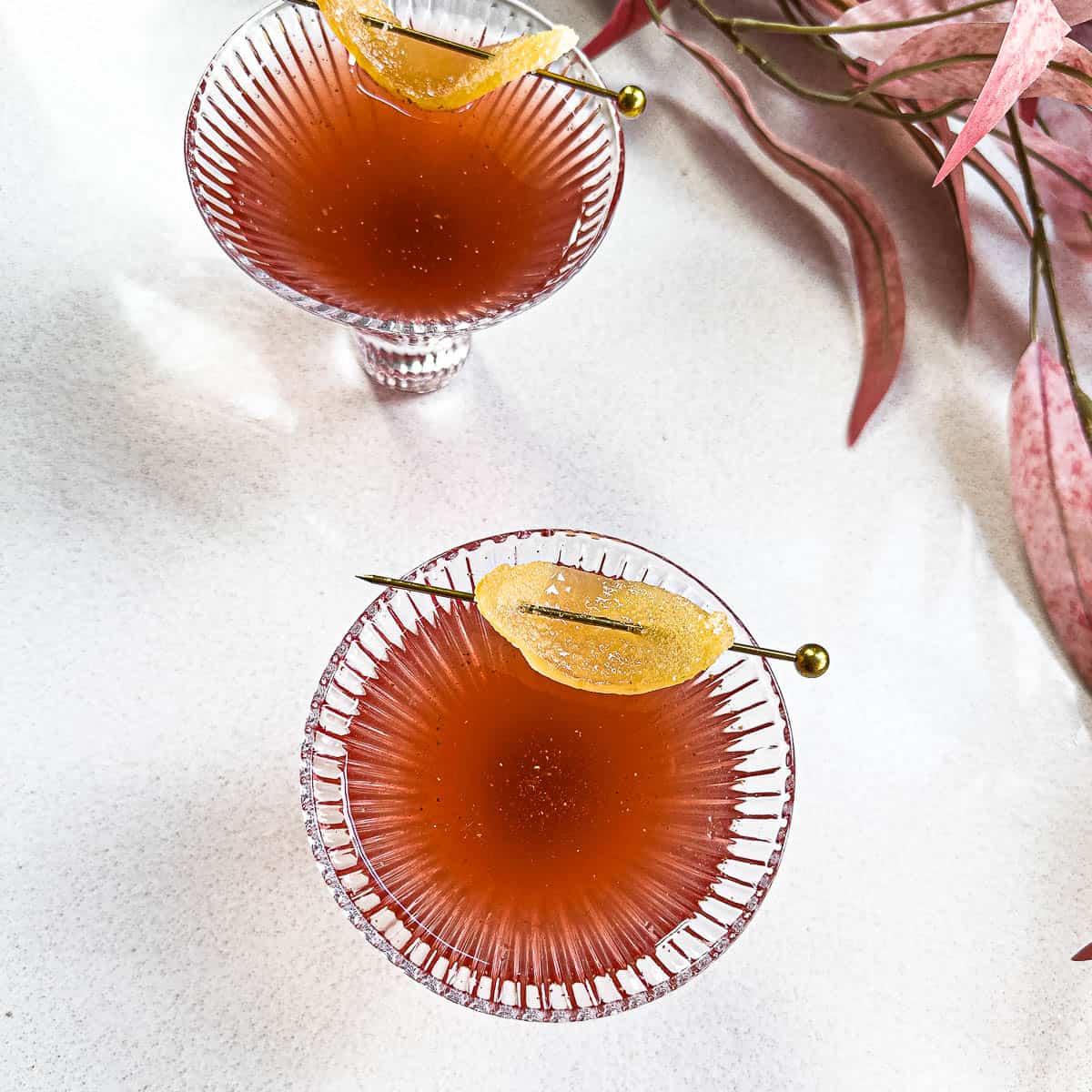 Two glasses of chaat spiced pomegranate mocktail with a candied ginger garnish.