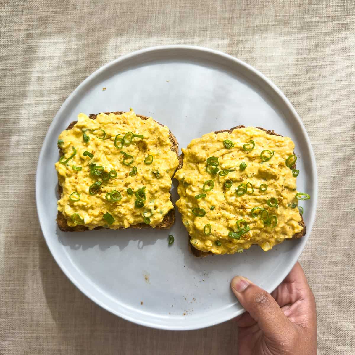 Curried egg salad with cottage cheese and green onions on top of toast on a gray plate.