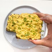 Curried egg salad with cottage cheese and green onions on top of toast on a gray plate.