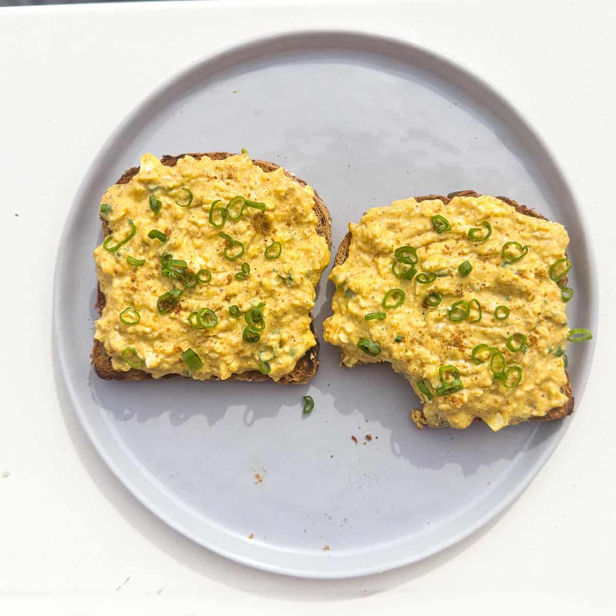 Curried egg salad with cottage cheese and green onions on top of toast on a gray plate.