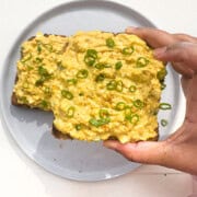 Curried egg salad with cottage cheese and green onions on top of toast on a gray plate.