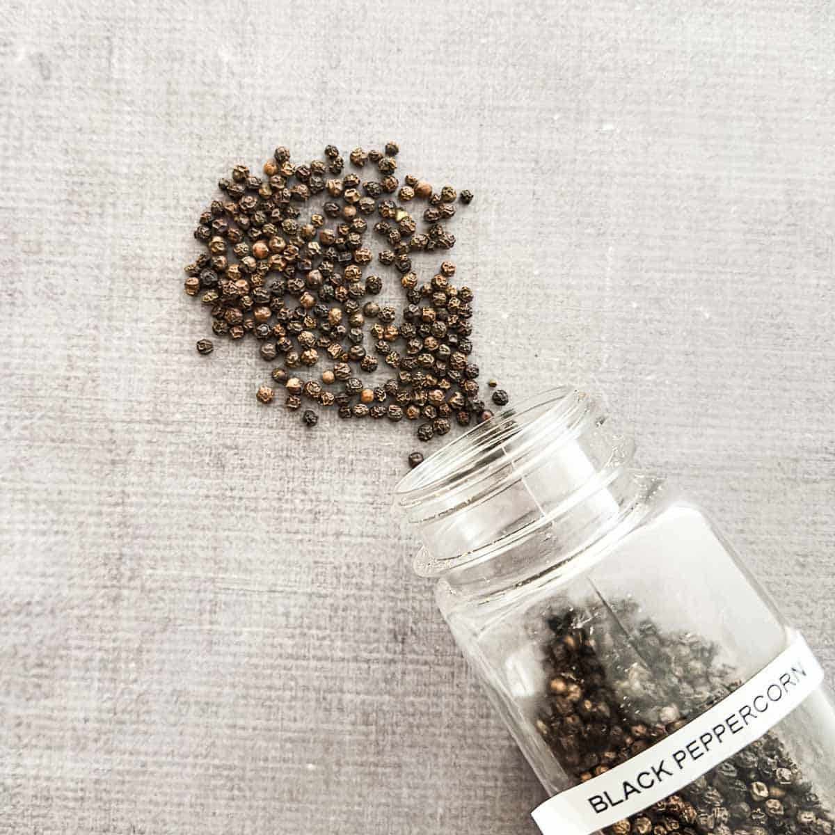 Black peppercorn poured out of a spice container.