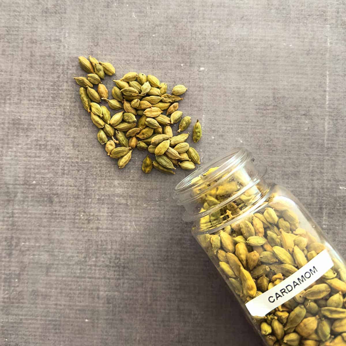 Green cardamom pods poured out of a spice container.