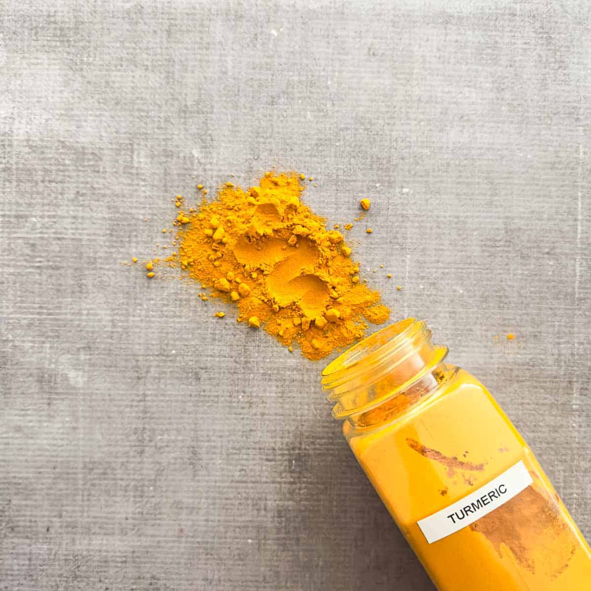 Turmeric powder poured out of a spice container.